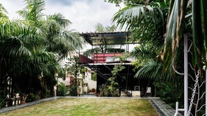 A courtyard with a covered outdoor area, surrounded by lush greenery and a clear sky.