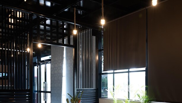 A modern interior with a glass-top table, leather sofa, potted plants, and hanging lights.