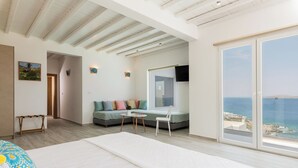 A bedroom with a large bed, a sofa with cushions, a small table, and a view of the sea through a large window. - 3-bedroom Infinity Blue villa in fantastic Sunset Views close to Mykonos Town (Mykonos)