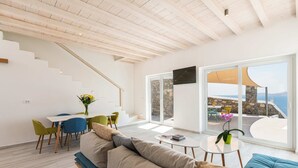 A modern living room with a staircase, a dining area, and a large window with a view. - 3-bedroom Infinity Blue villa in fantastic Sunset Views close to Mykonos Town (Mykonos)