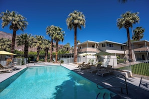 A swimming pool with lounge chairs and umbrellas, surrounded by palm trees and a building with balconies. - Pied-à-terre by Albert Frey (Palm Springs)