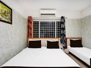 A room with two beds, a window with a grid pattern, an air conditioner, and a painting on the wall. - Suiteporur Formerly Jeya's Elite (Chennai)