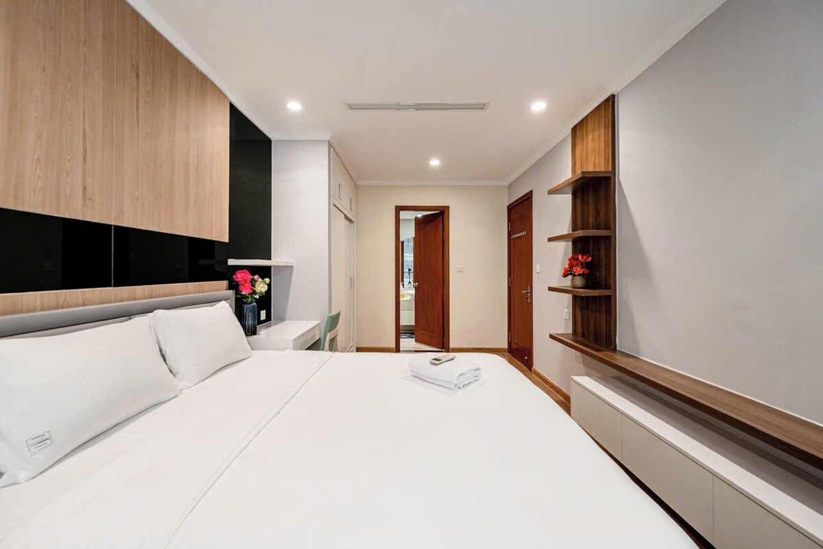 A modern hotel room with a large bed, built-in wardrobe, bedside tables, and a view into the hallway.