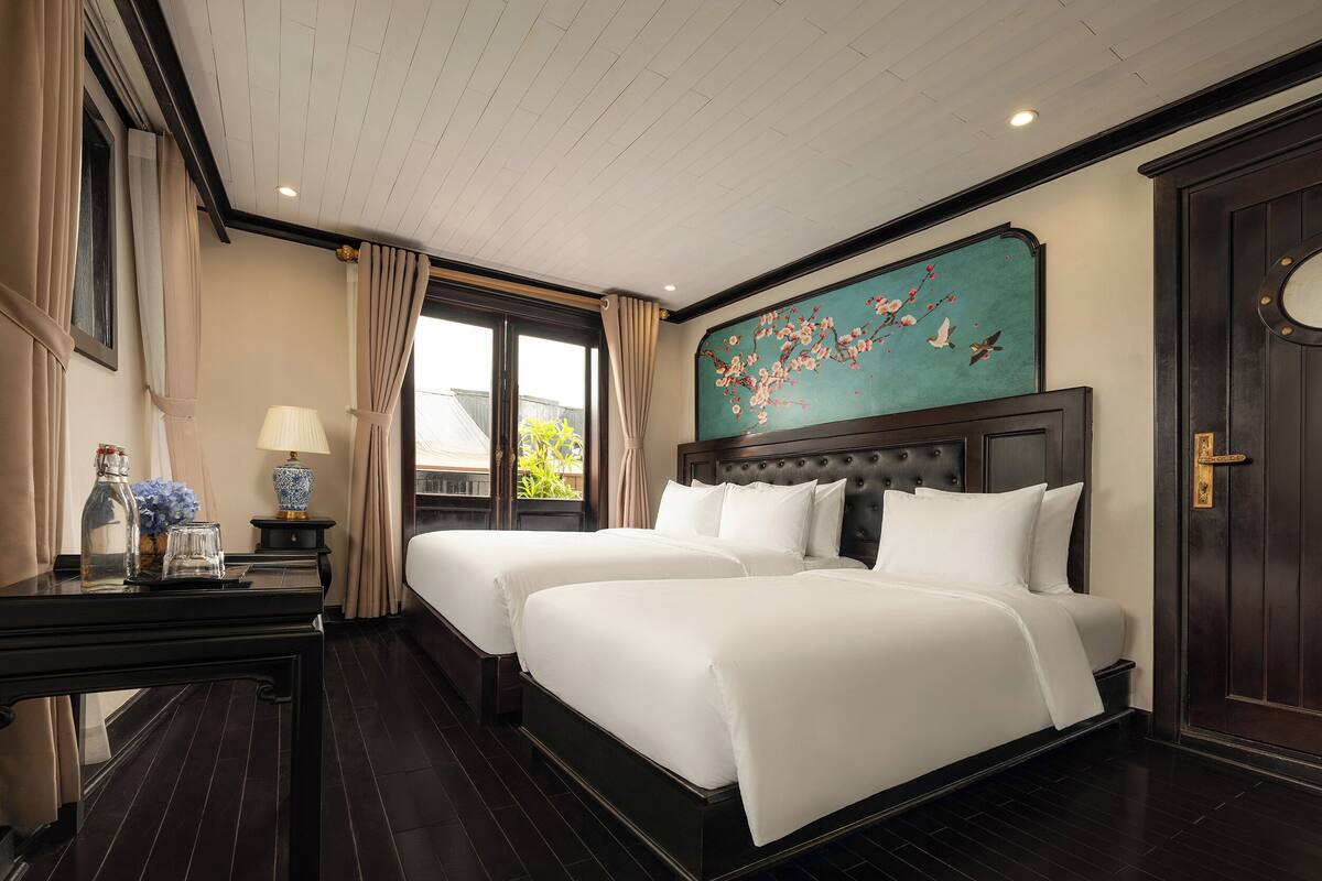 Quarto de hotel com uma cama grande, uma escrivaninha com abajur, uma janela com cortinas e um quadro na parede.