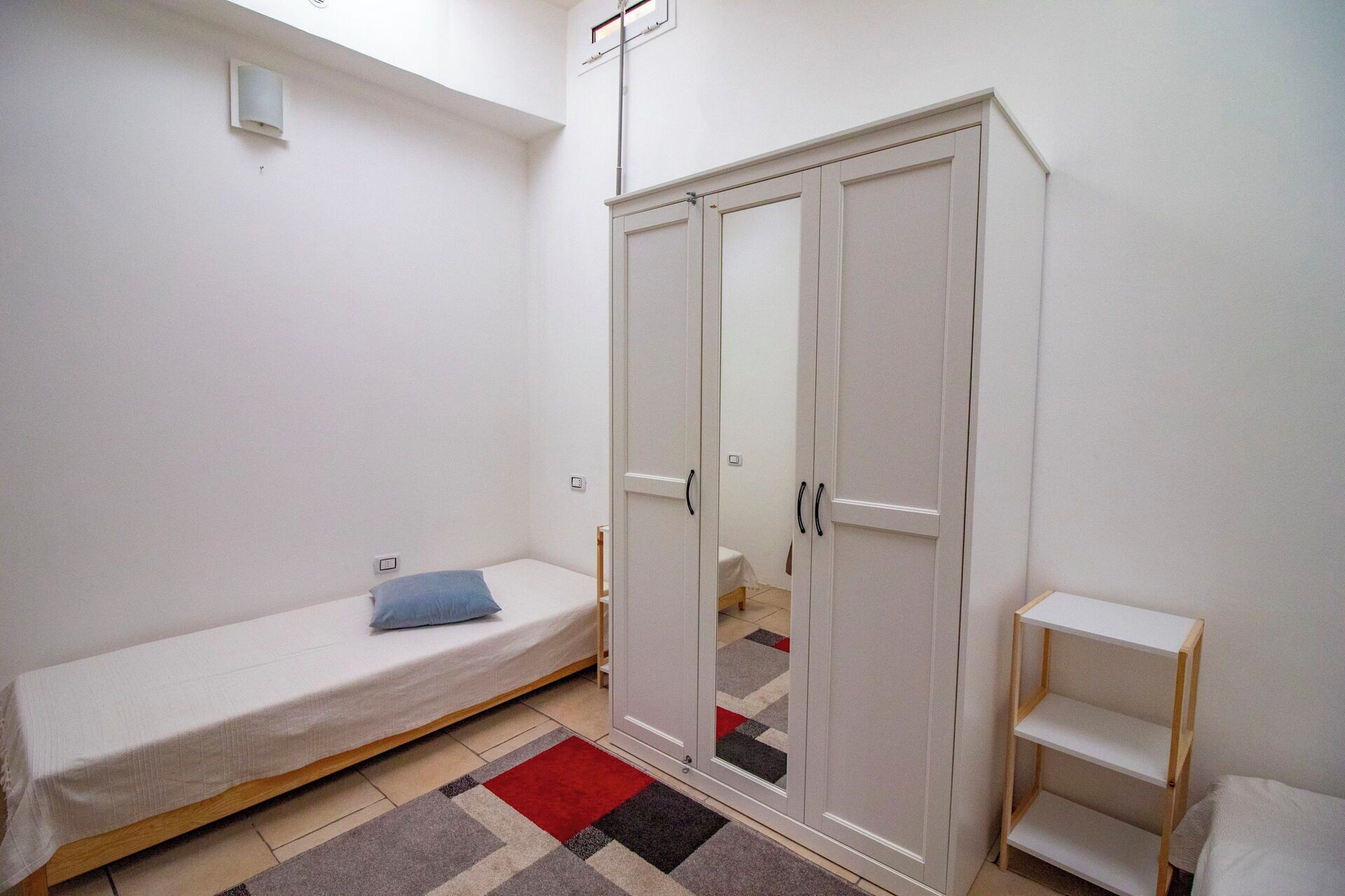 A small, single-room apartment with a bed, wardrobe, and a small table.