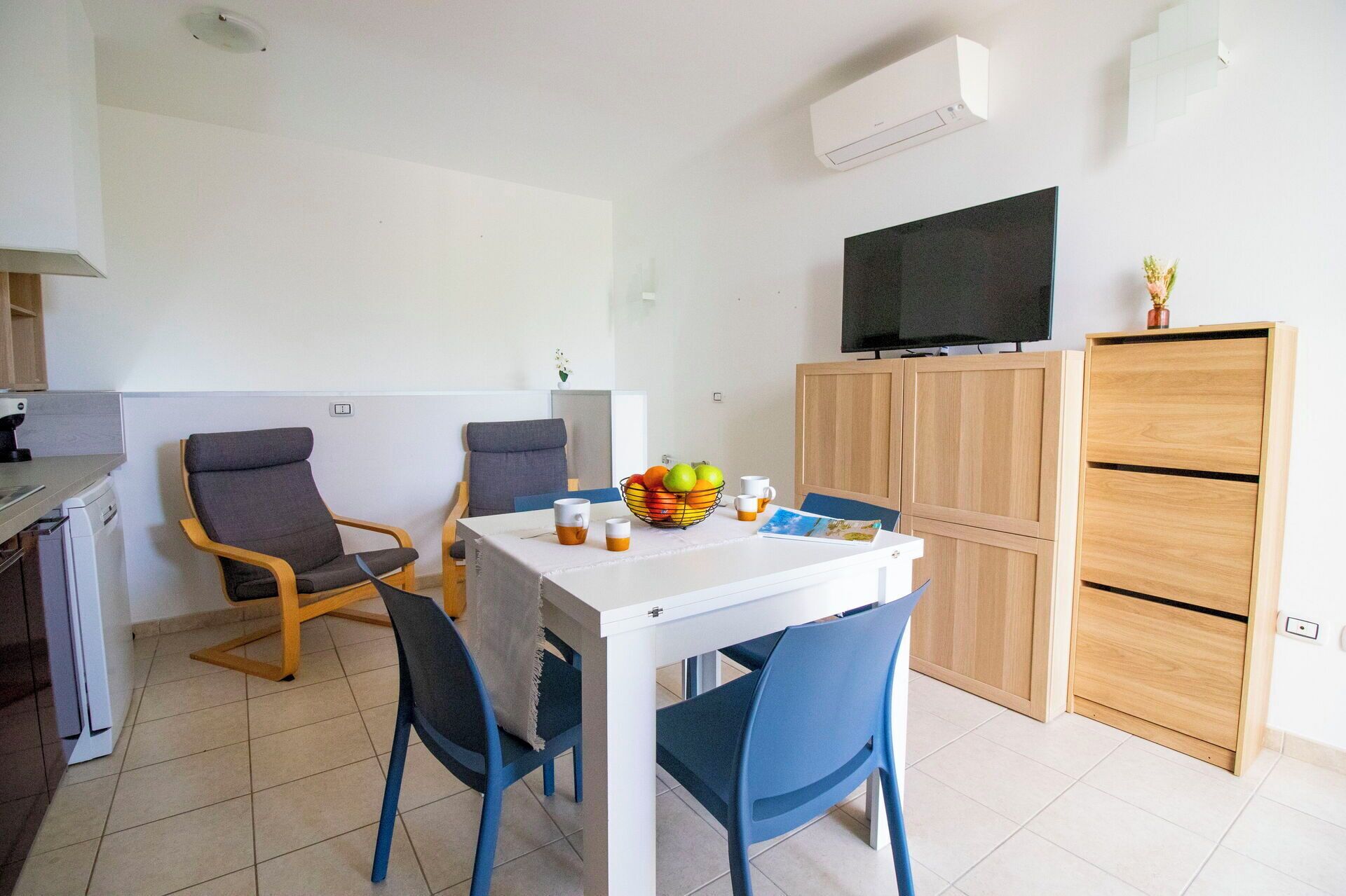 Ein kleiner, moderner Raum mit Esstisch, zwei Stühlen, einem Fernseher und einem Schrank.