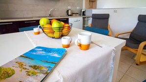 Una cocina con un frutero, dos tazas y una revista sobre una mesa.