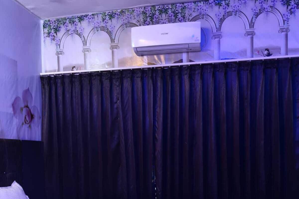 A hotel room with a bed, a sofa, a marble-patterned floor, a wall-mounted air conditioner, and a floral wallpaper design.