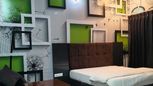 A modern bedroom with a bed, a nightstand, a chair, and a decorative wall with geometric patterns and green accents. - Amrit Hotel & Resort (Thanagazi)