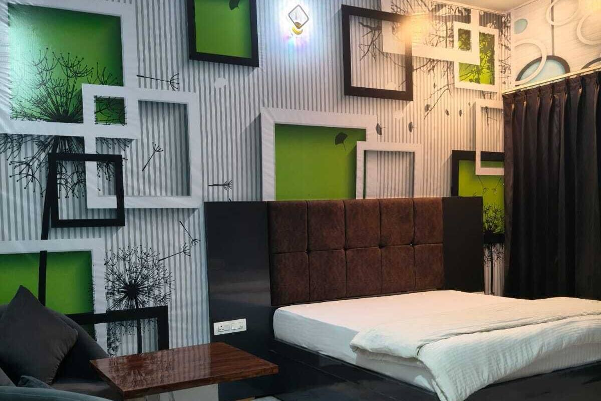 A modern bedroom with a bed, a nightstand, a chair, and a decorative wall with geometric patterns and green accents.