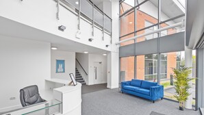 A reception area with a glass desk, a blue sofa, and a staircase leading to an upper level. - Beautiful 1-bedroom apartment in the heart of Birmingham (Birmingham)