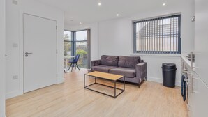 A modern living room with a sofa, a coffee table, a window with blinds, and a door. - Beautiful 1-bedroom apartment in the heart of Birmingham (Birmingham)