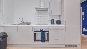 A modern kitchen with white cabinetry, a stainless steel range hood, a built-in oven, and a coffee maker. - Beautiful 1-bedroom apartment in the heart of Birmingham (Birmingham)
