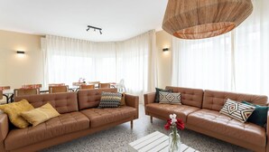 Een moderne woonkamer met twee bruine leren banken, een witte salontafel en een hanglamp.