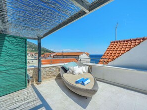 Ein Balkon mit Korbstuhl, Blick aufs Meer und ein Ziegeldach.