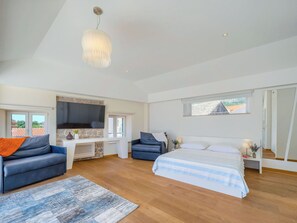 Ein geräumiges Schlafzimmer mit einem großen Bett, einer Sitzecke mit einer Couch, einem Schreibtisch und einem Fernseher.