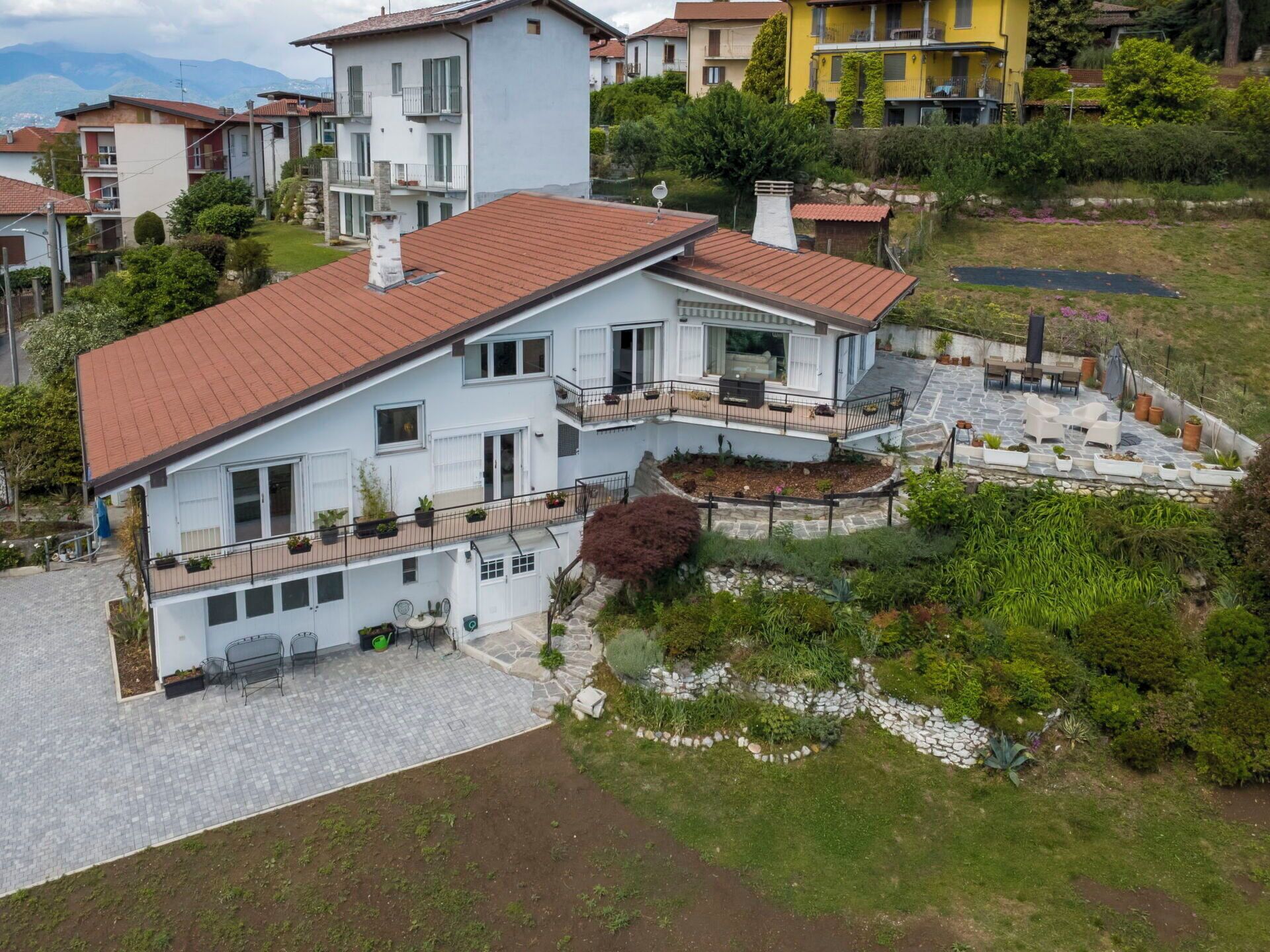 A multi-story house with a red-tiled roof, a stone patio, and a garden area with plants and a small pond.