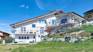 Una casa a due piani con un balcone, un muro di sostegno in pietra e un giardino con diverse piante.