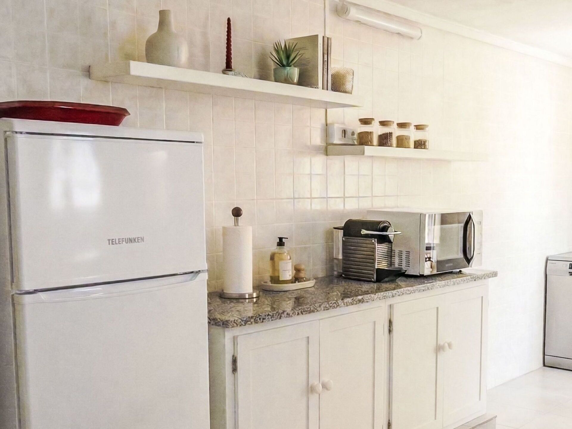 Eine Küche mit weißen Schränken, einem weißen Kühlschrank, einer Mikrowelle und einer Kaffeemaschine auf der Arbeitsplatte.