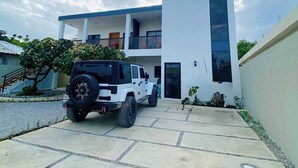 A modern two-story building with a white exterior and a large glass window. A white SUV is parked in the driveway. - Casa Brisa Caribe Cabrera Perfect for Family & Friends (Cabrera)