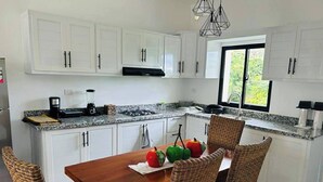 A kitchen with white cabinets, a granite countertop, a dining table with wicker chairs, and a window with a view of greenery. - Casa Brisa Caribe Cabrera Perfect for Family & Friends (Cabrera)