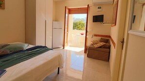 Habitación de hotel con una cama, un pequeño espacio de descanso con una mesa, un refrigerador y un televisor montado en la pared.