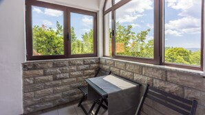 Una habitación de esquina con pared de piedra, dos ventanas, una mesa y un banco.