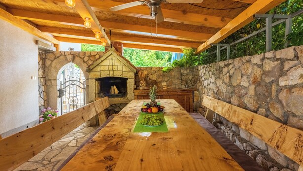 Un área de comedor al aire libre con chimenea de piedra, bancos de madera y una mesa de madera con fruta.