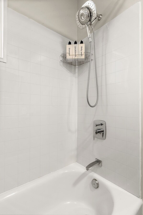 Een badkamer met een witte betegelde douche, een badkuip en een plank met toiletartikelen.