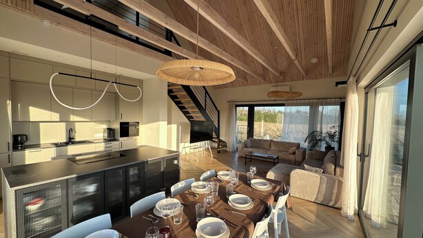 A modern kitchen with a central island, a dining area with a table set for six, and a living space with a sofa and a large window. - Stylish Japandi Home | Sleeps 8 | Bathrooms 2 | Garden (Kołczewo)