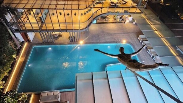 A swimming pool with a person diving, lounge chairs, and a covered area with tables and chairs. - BluSalzz Collection Casa Onze Goa (Calangute)