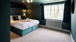 A bedroom with a bed, a window with curtains, a radiator, and a wall-mounted light fixture. - Daisy Cottage | Sands Farm (Wilton)