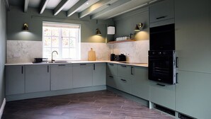 A modern kitchen with grey cabinets, a built-in oven, and a window providing natural light. - Daisy Cottage | Sands Farm (Wilton)
