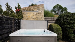 A hot tub in a backyard with a stone wall, wooden fence, and greenery. - Daisy Cottage | Sands Farm (Wilton)