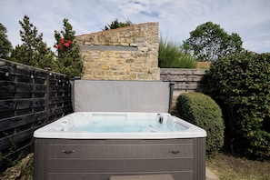 Ein Whirlpool in einem Garten mit Steinmauer, Holzpforte und viel Grün.
