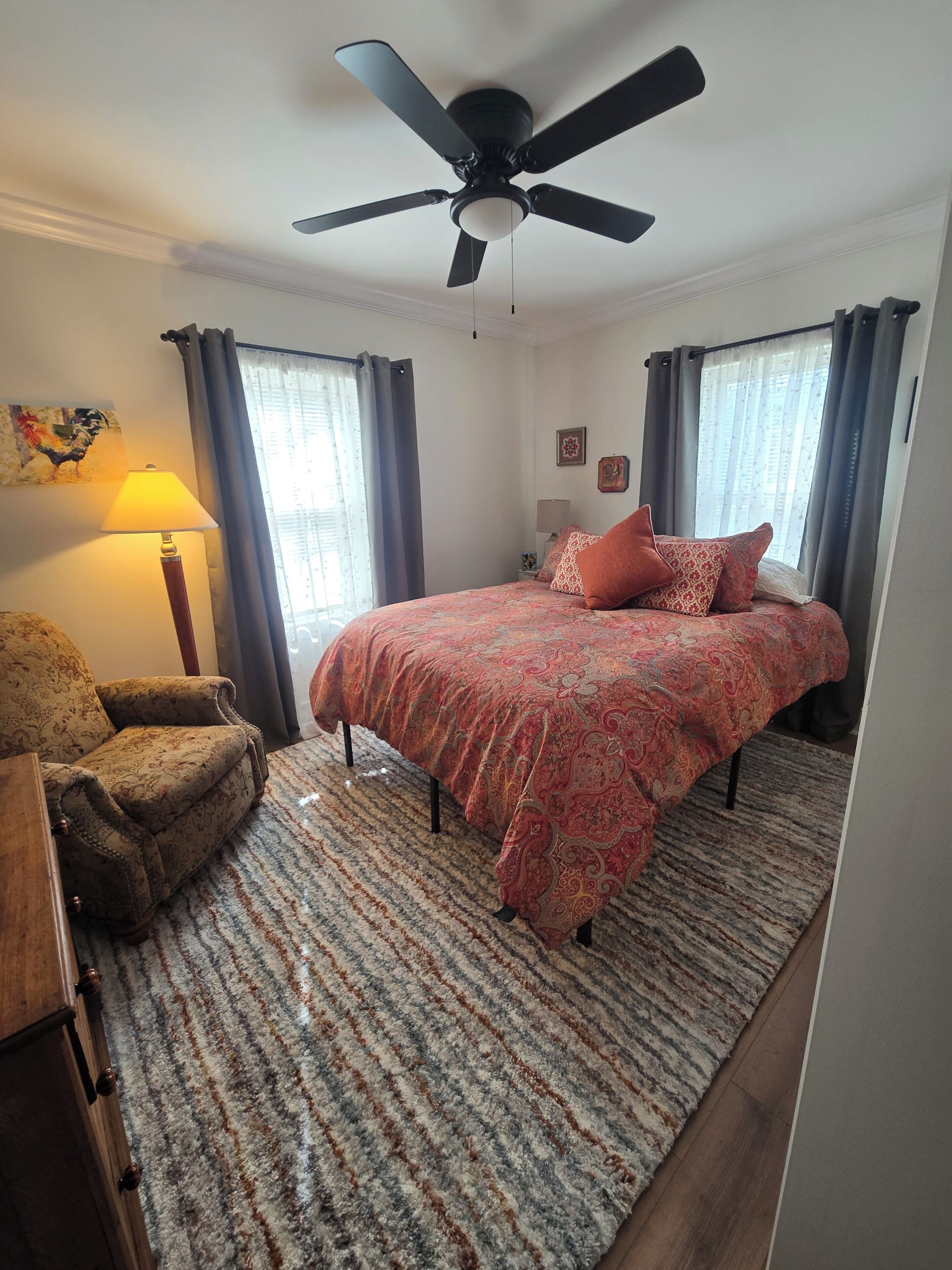 Une chambre à coucher avec un lit, une chaise, un ventilateur de plafond et une lampe.