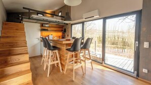 A modern kitchen with a dining area, wooden flooring, and large windows. - Tiny House an Zwei Naturteichen - Ruhe, Kamin & Terrasse Nahe Dresden - Best Price! (Grossharthau)
