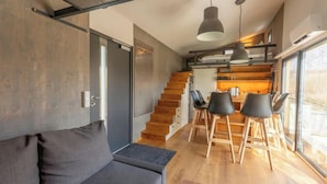 A modern interior with a sofa, dining table, chairs, and a staircase. - Tiny House an Zwei Naturteichen - Ruhe, Kamin & Terrasse Nahe Dresden - Best Price! (Grossharthau)
