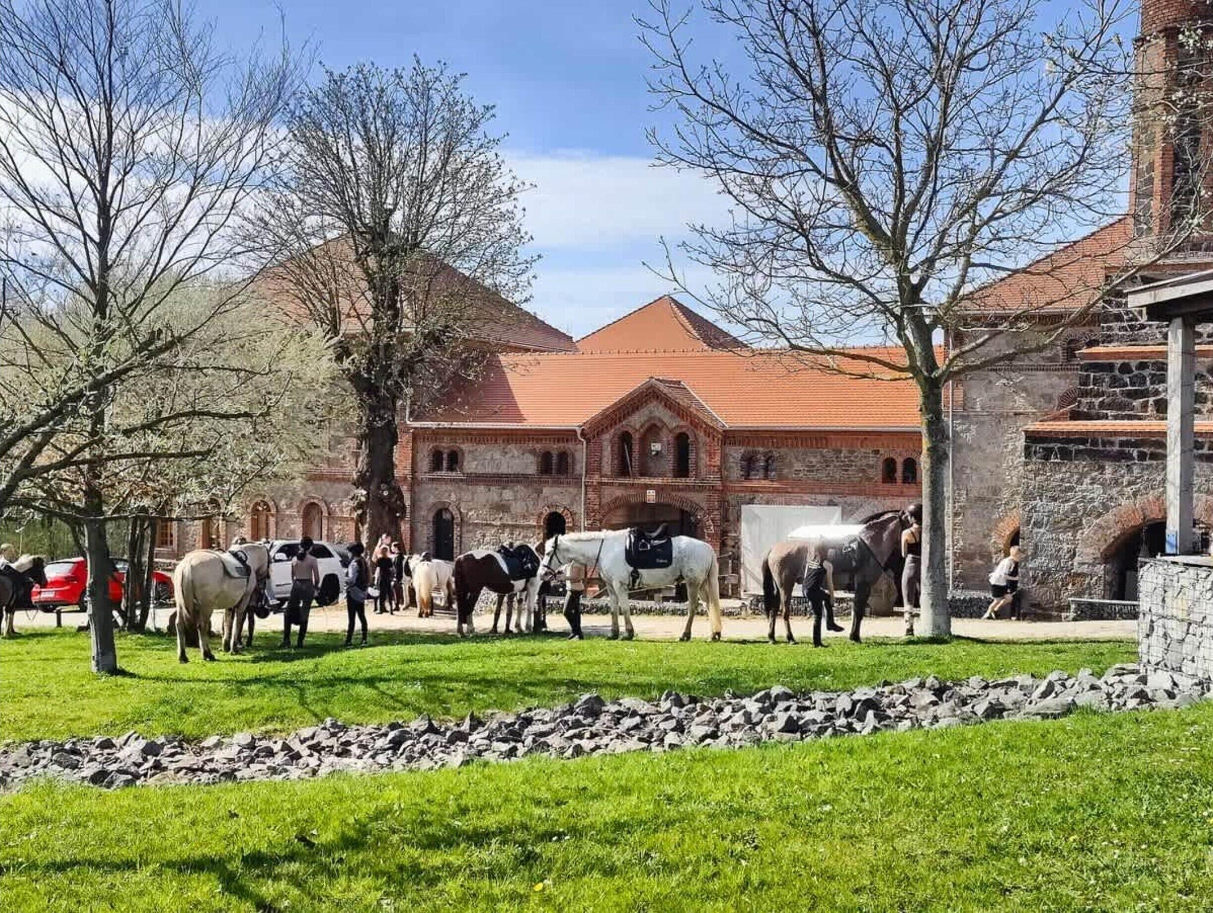 A historic building with a red-tiled roof, surrounded by a grassy area with horses.