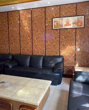 A modern living room with a black leather sofa, a wooden coffee table, and a decorative wall panel.