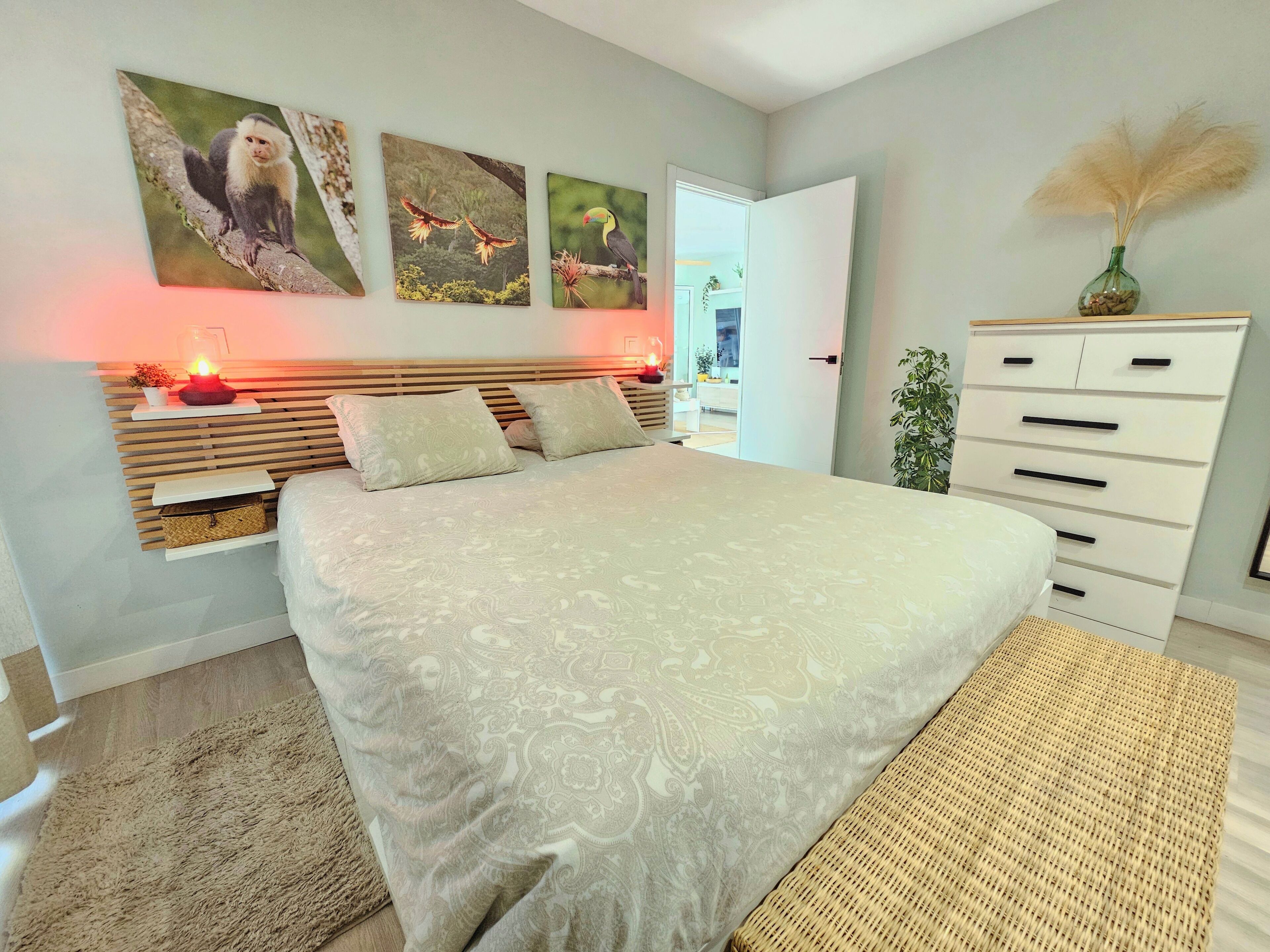 A bedroom with a bed, bedside tables, a dresser, and wall art.