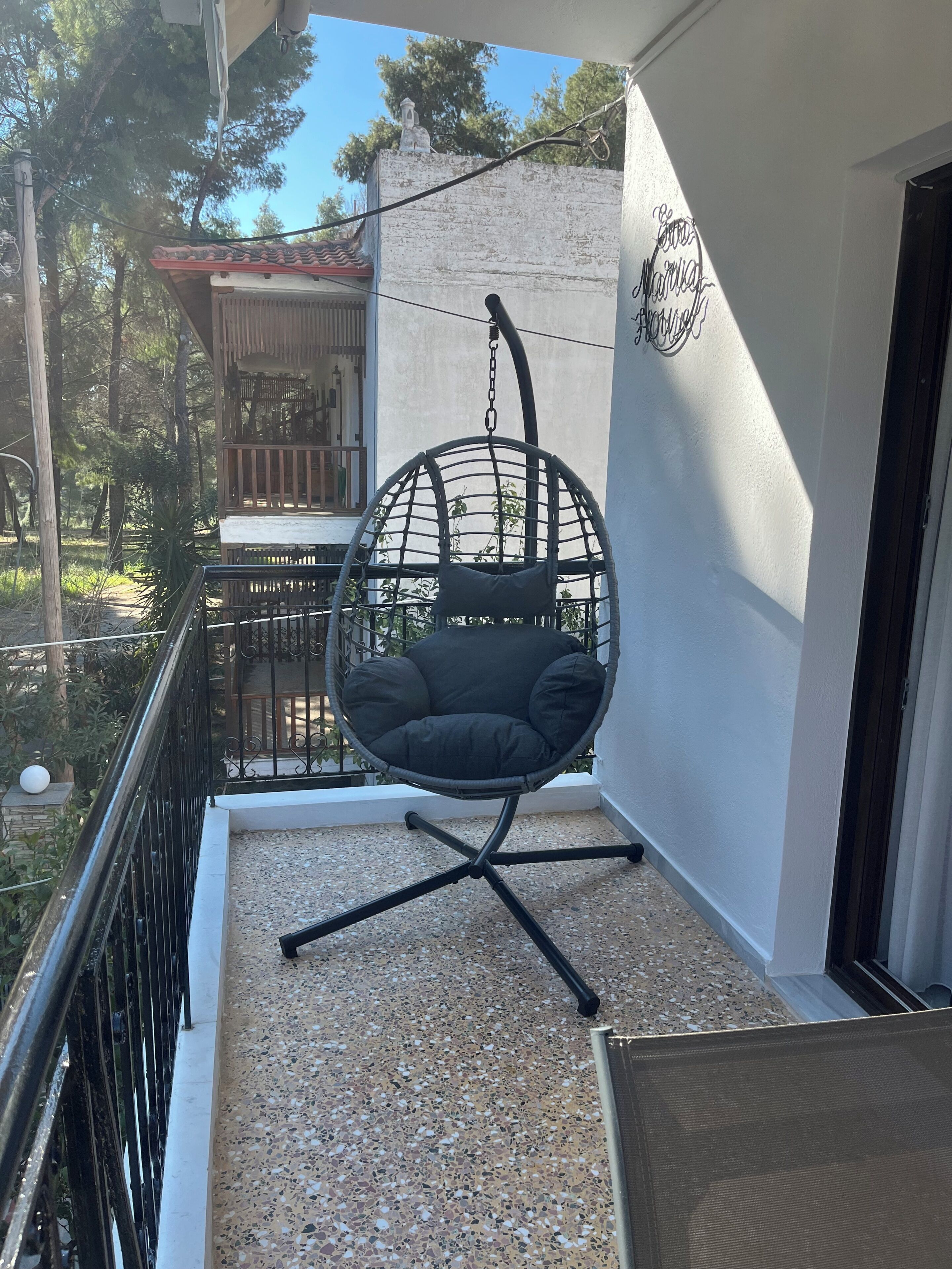 A balcony with a hanging chair, a small table, and a view of a building with a balcony.