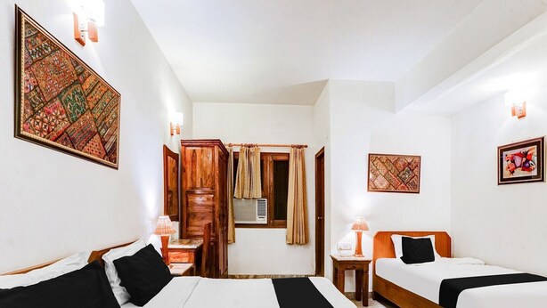Ein Hotelzimmer mit zwei Betten, einem Holzschrank, einem kleinen Tisch mit Lampe und dekorativen Wandbildern.