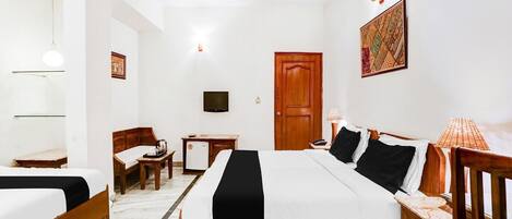 Una habitación de hotel con cama, mesitas de noche, escritorio, silla, ventilador de techo, televisor y puerta.