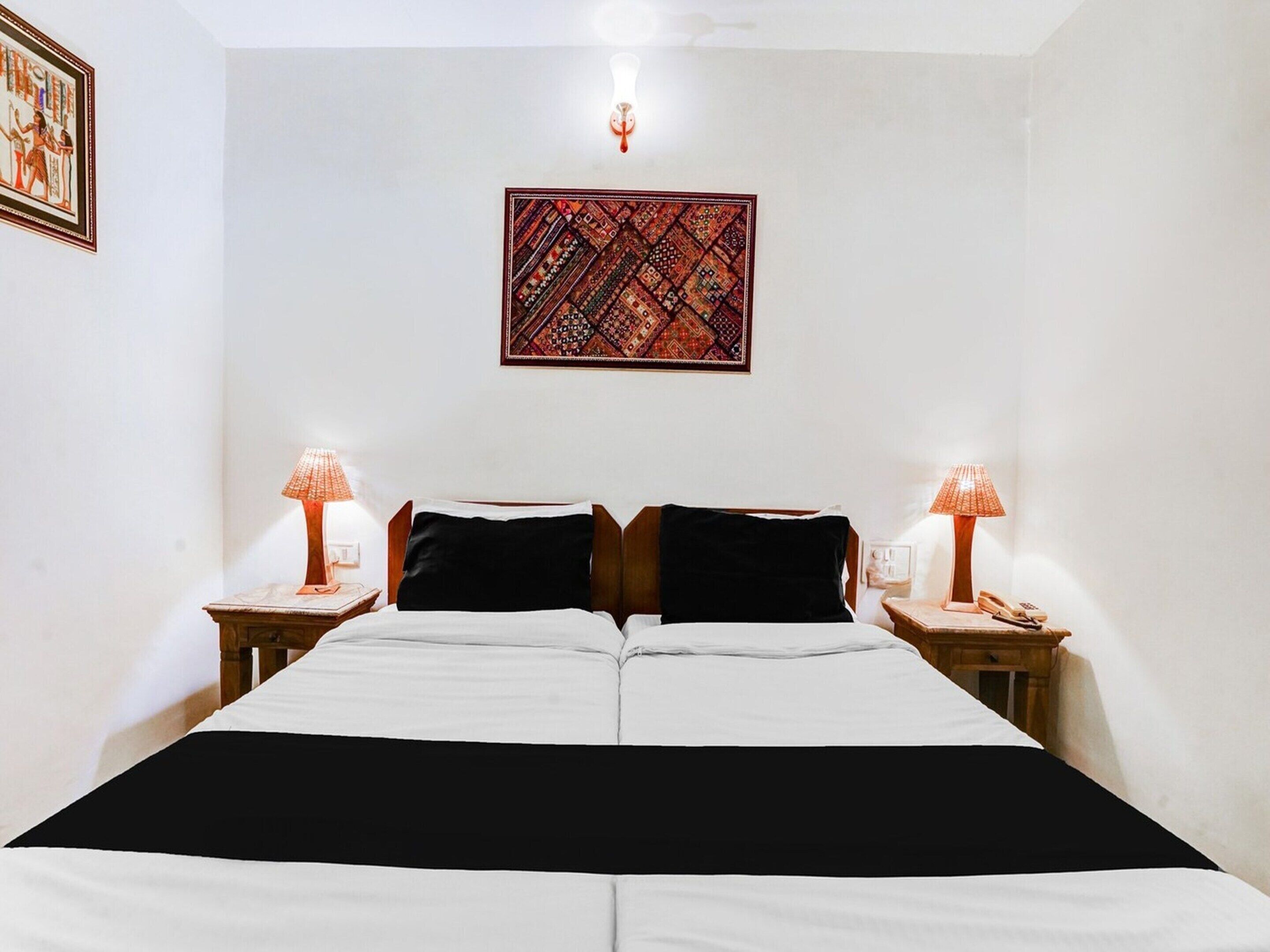 A double bed with black and white bedding, two bedside lamps, a wall hanging, and a small table with a phone.