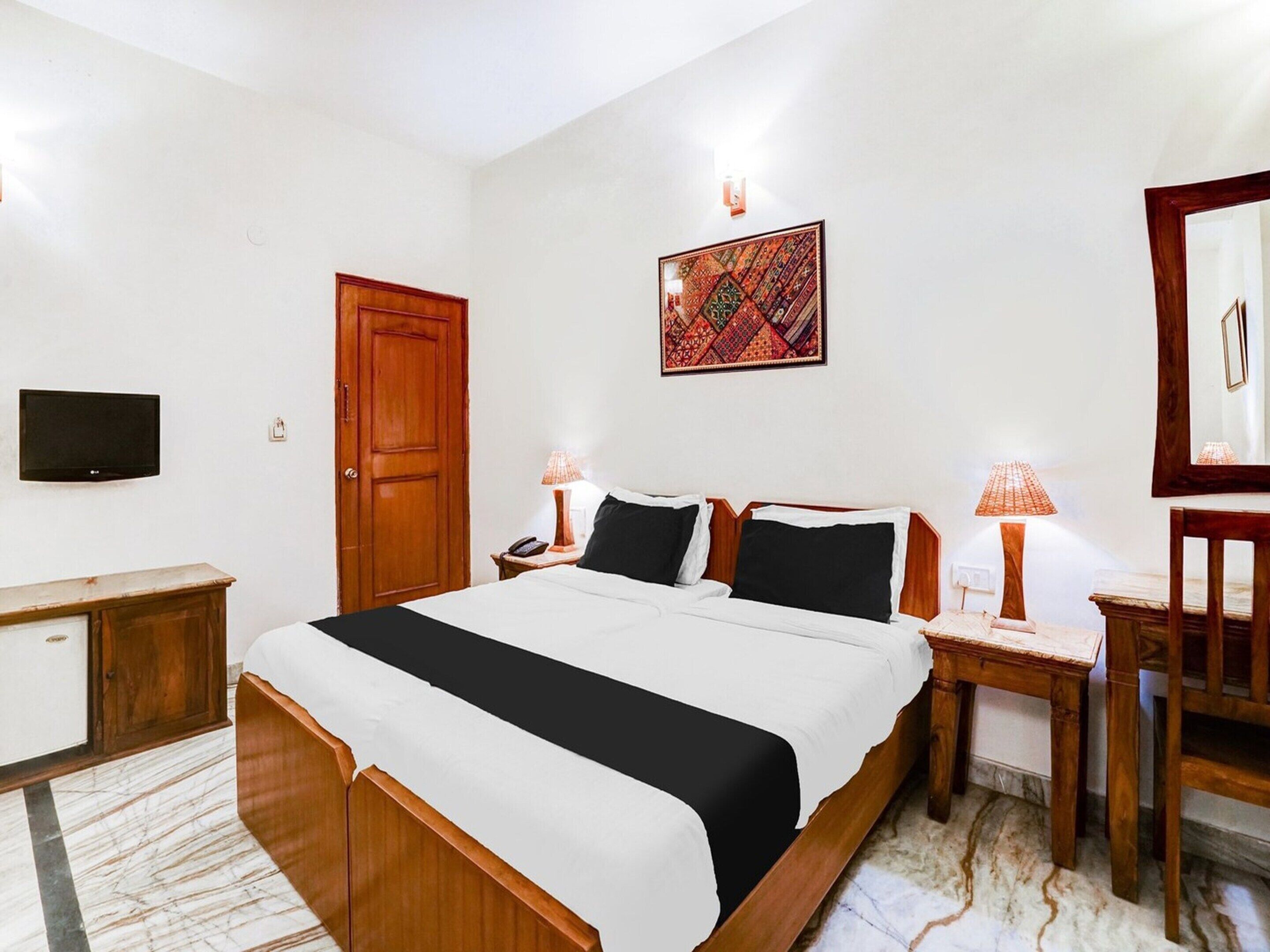 A hotel room with a bed, bedside lamps, a TV, a door, and a wall-mounted artwork.