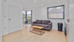 Una sala moderna con un sofá, una mesa de centro, una ventana con persianas y una puerta.