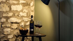 Una botella de vino, dos copas de vino y un bol de aperitivos sobre una mesa frente a un muro de piedra.