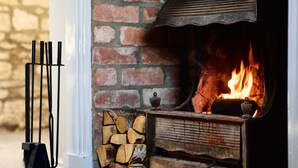 Una chimenea con leña, una reja de metal y un muro de ladrillo.