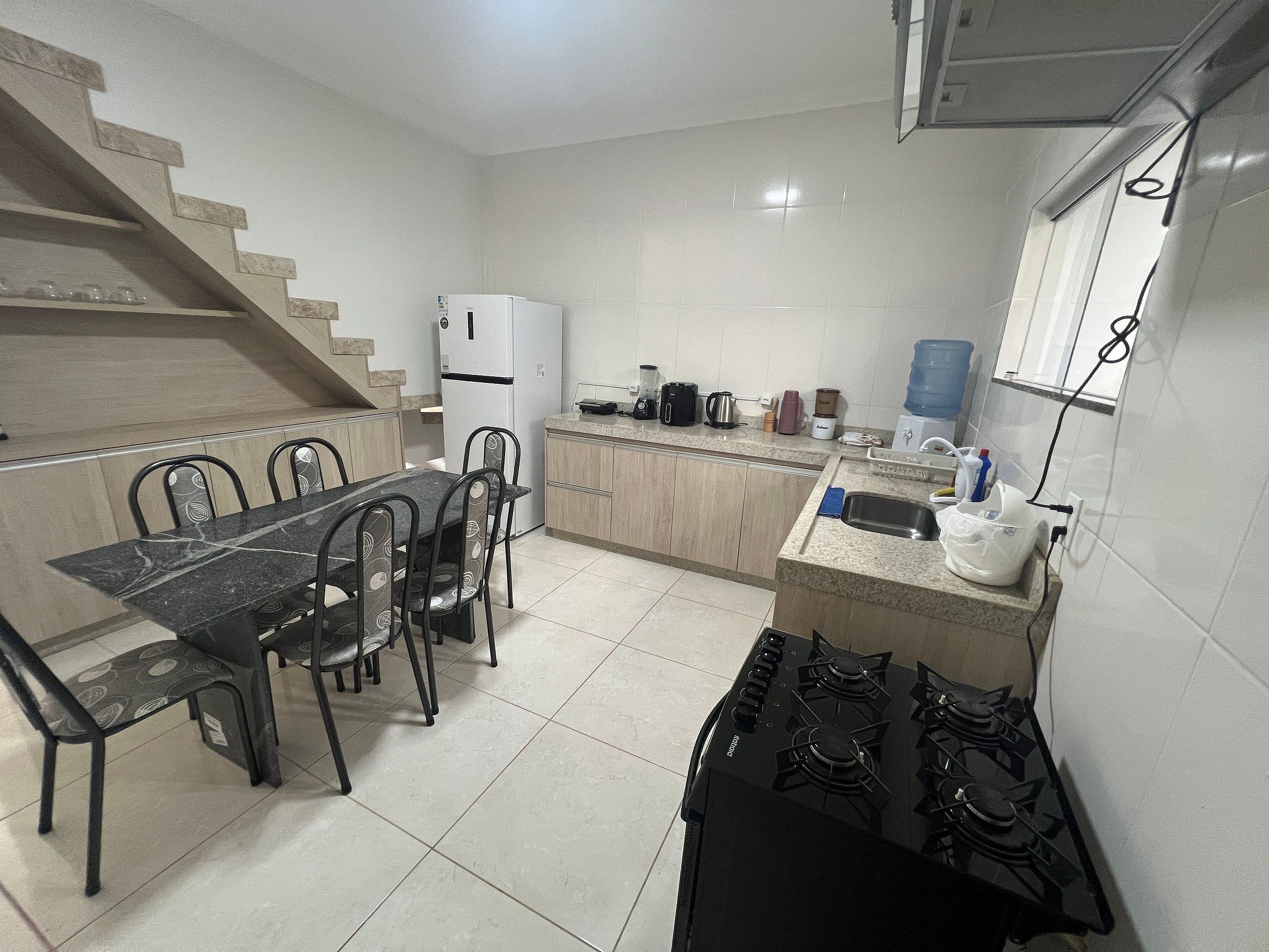 A compact kitchen with a dining table, chairs, a refrigerator, a stove, and a water dispenser.